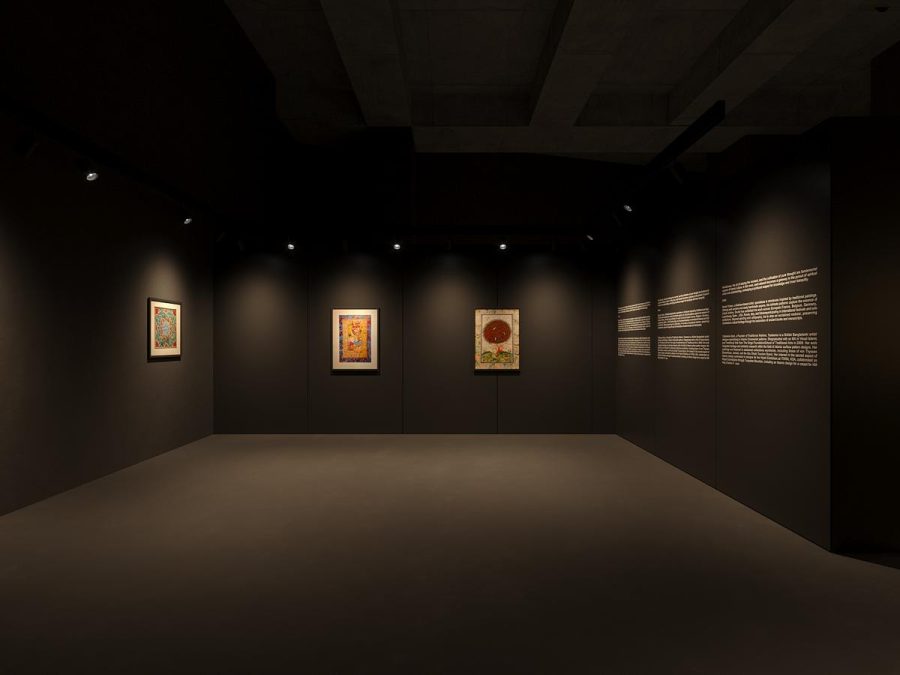 Framed miniature paintings hung on dark walls under warm spotlights
